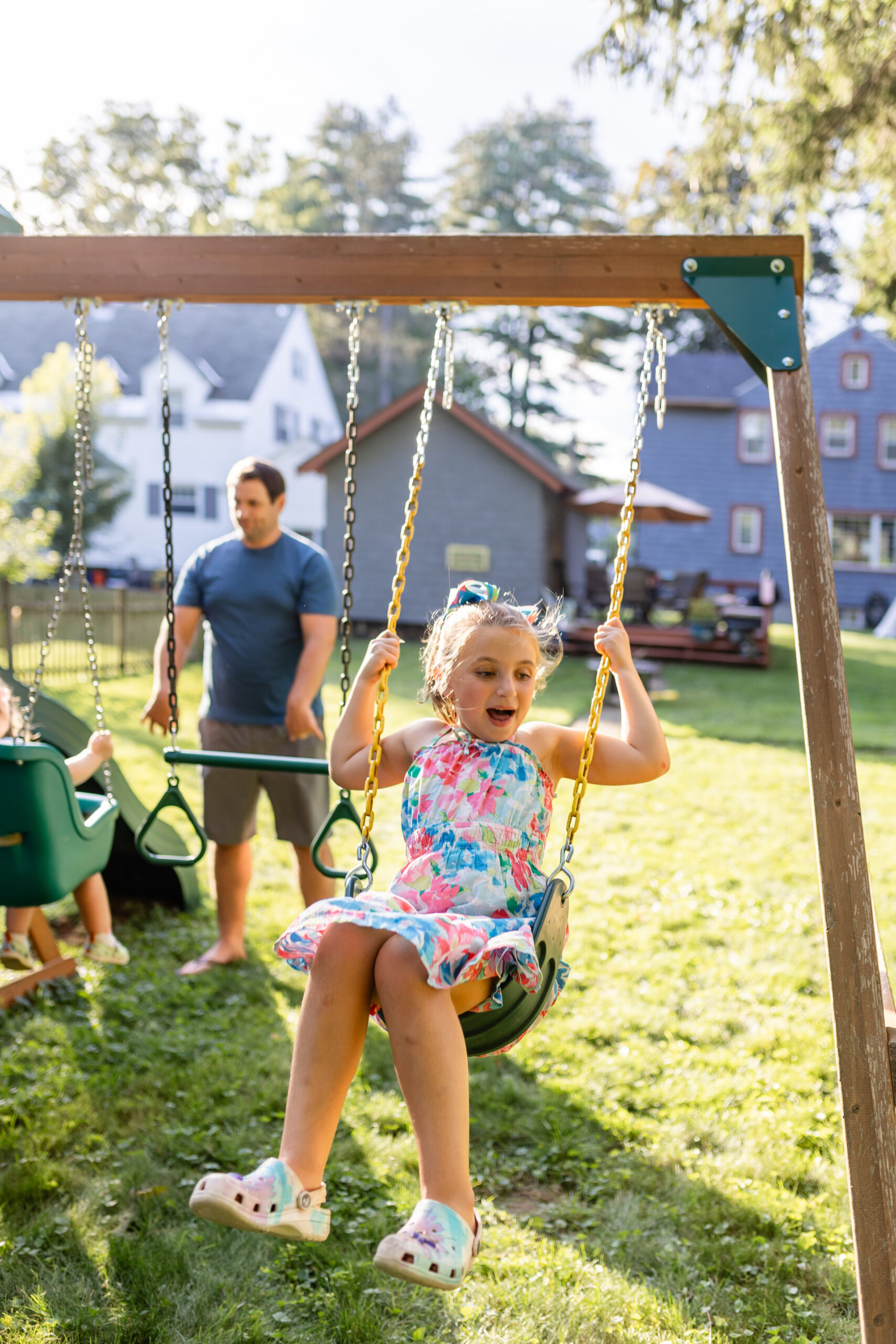 A carefree summer backyard family session with an Albany family, featuring children playing on the swings