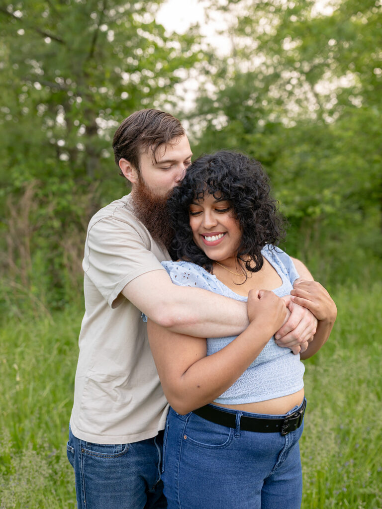 Couple wrapping arms around each other in a green field