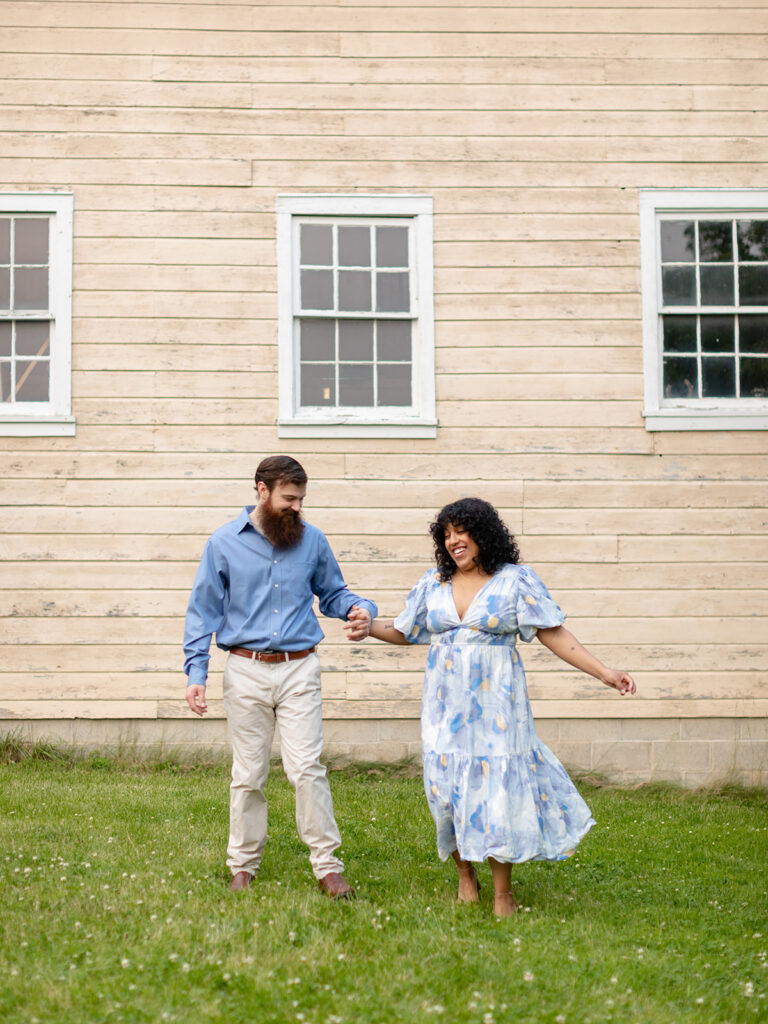 Couple dancing in a field in front of a rustic tan barn