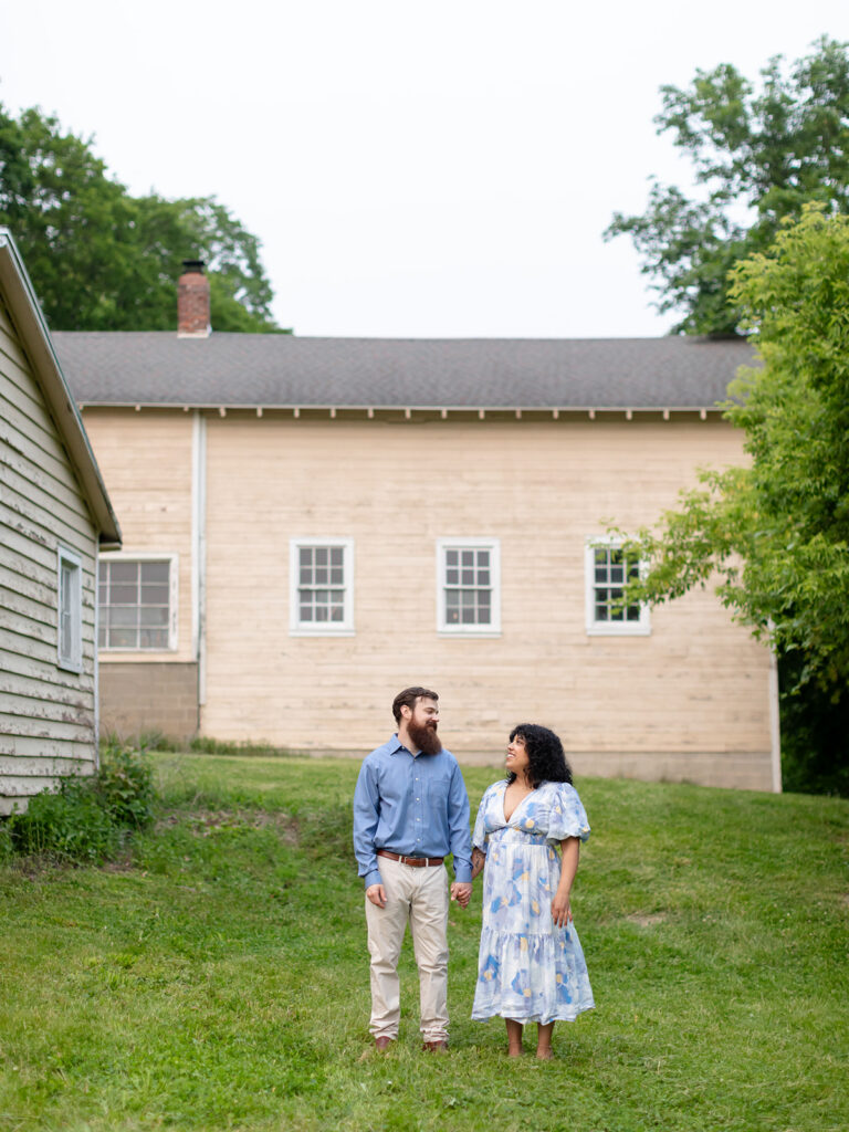 Couple standing and looking at each other in a field with a rustic barn in the background